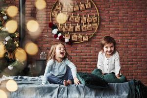 Loud laughing. Little girls having fun on the bed with holiday interior at the background photo