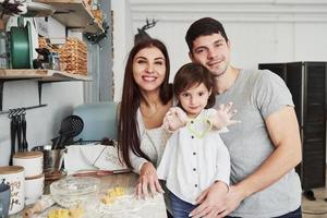 chica mostrando forma de cocción en forma de corazón. cerca de la mesa de la cocina. linda familia posando para la foto