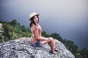 mirada satisfecha. Atractiva chica turística posando en el borde de la montaña con un lago de agua clara en segundo plano.
