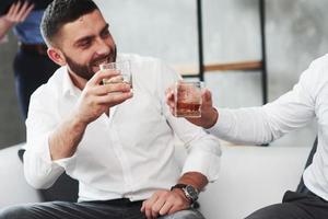 Dos colegas celebrando un buen negocio en su negocio bebiendo alcohol.