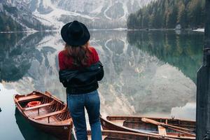 mira esta agua limpia. Mujer con sombrero negro disfrutando del majestuoso paisaje de montaña cerca del lago con barcos foto