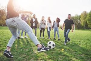 un grupo de amigos en ropa casual juega al fútbol al aire libre. la gente se divierte y se divierte. descanso activo y puesta de sol escénica foto