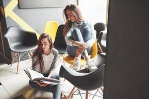 Two beautiful twin girls spend time read a book in library in the morning. Sisters relaxing in a cafe and having fun together photo