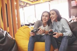 Twin sister sisters play on the console. Girls hold joysticks in their hands and have fun photo