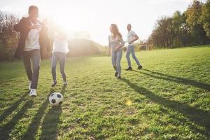 A group of friends in casual outfit play soccer in the open air. People have fun and have fun. Active rest and scenic sunset photo