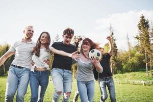 un grupo de amigos en ropa casual juega al fútbol al aire libre. la gente se divierte y se divierte. descanso activo y puesta de sol escénica foto