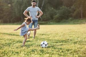 así es como funciona. Papá entusiasta le enseña a su hija cómo jugar su juego favorito. es fútbol y hasta las niñas pueden jugarlo foto