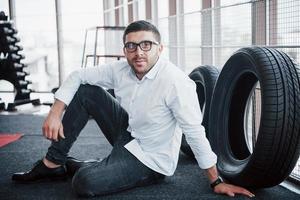 A handsome young boy sitting on the floor in the gym, in a white shirt and pants. Concept of sport photo