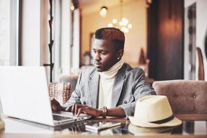 Retrato de hombre afroamericano sentado en un café y trabajando en un portátil. foto