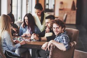 Group of creative multietnic friends sitting at wooden table. People having fun while playing board game photo