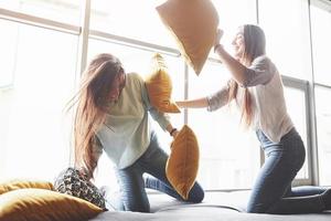 dos hermosas hermanas gemelas jóvenes pasan tiempo juntas y están luchando con almohadas. hermanos que se divierten en el concepto de casa foto