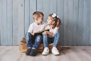 listo para grandes viajes. feliz niña y niño leyendo un libro interesante con un maletín grande. concepto de libertad e imaginación foto