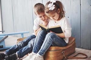 Ready to big travel. Happy little girl and boy reading interesting book carrying a big briefcase. Freedom and imagination concept photo