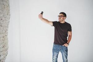 Playful bearded man making selfie on smartphone and white wall background photo