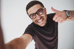 Retrato de un hombre sonriente con gafas mostrando el pulgar hacia arriba sobre fondo blanco. foto