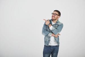 Happy excited bearded man in eyeglasses looking at camera with smile and pointing away at copy space with two fingers isolated over white background photo