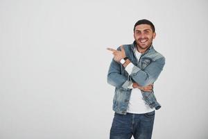 Happy excited bearded man in eyeglasses looking at camera with smile and pointing away at copy space with two fingers isolated over white background photo