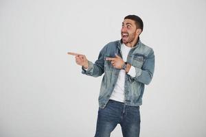 Happy excited bearded man in eyeglasses looking at camera with smile and pointing away at copy space with two fingers isolated over white background photo