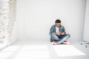 A guy in casual clothes is sitting at home in an empty apartment holding a credit card and calling on the phone. Maybe he's a new resident and has not bought any furniture yet. photo