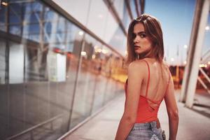 hermosa chica sexy turista caminando en la concurrida calle de la ciudad cerca del aeropuerto. Mujer mirando a la cámara al aire libre vistiendo una camiseta roja de moda foto