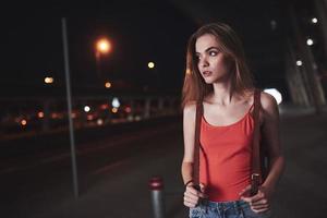 A young beautiful girl with a backpack behind her shoulders stands on the street near an airport or a railway station on a warm summer evening. She just arrived and waits for a taxi or her friends photo