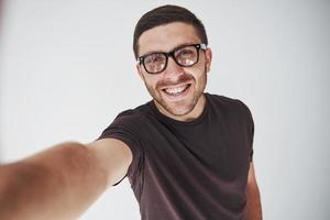 Chico joven inconformista con gafas riendo felizmente aislado sobre fondo blanco. foto