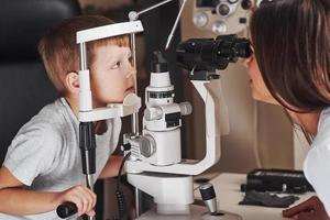 This might take one more minute. Little boy have test for his eyes with special optical apparatus by female doctor photo