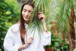 Feel the nature. Gorgeous young woman holding the branch in the greenhouse