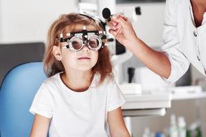 Now I will close one eye. Doctor checking little girl sight and tuning the phoropter photo