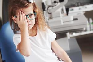 cierre el ojo derecho con la mano. niña revisando su visión con nuevas gafas verdes foto