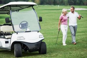 The golf cart with lovely couple walking near the vehicle and smiling photo