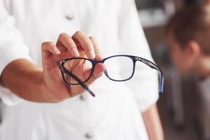 Kid at background. Woman hands holds the blue eyeglasses in the doctor cabinet photo