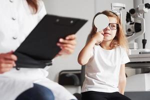 Kid struggles to read those words. Woman with documents tests the visual acuity of little girl photo