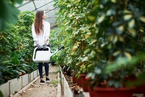 Young girl walks between plants in the greenhouse and holds watering can photo