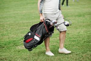 Foto recortada del hombre sujetando la bolsa con palos de golf mientras camina sobre el césped verde