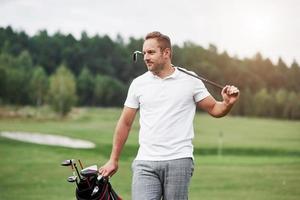 Portrait of walking golf player in the lawn and equipment in hands. Woods at background