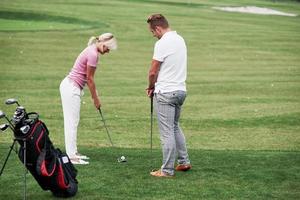 Adult man teaching the woman how to play the golf on the field with green grass photo