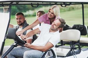 conducción extrema. amigos de la familia que se divierten montando el carrito de golf en el campo después del juego foto