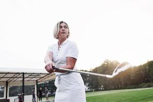 buscando nuevos logros. Foto de hermosa mujer adulta rubia sosteniendo un palo de golf en el campo deportivo verde
