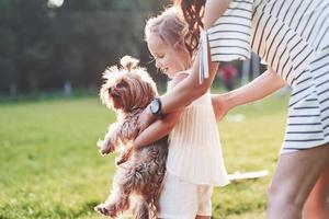 vista de cerca. Madre e hija jugando con un lindo perro afuera en la hierba verde foto