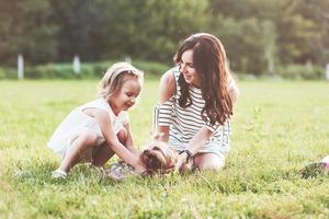 Mother and daughter playing with cute dog outside in the green grass