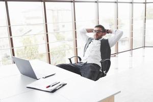 Young businessman having a rest while sitting in chair in the clean room and watching to the laptop photo