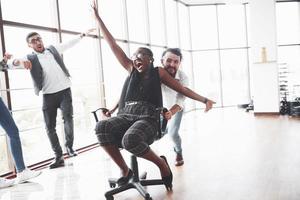 Young people having fun in the spacey office room riding the afro american oman on the chair photo