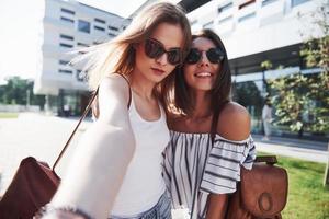 Two beautiful girls with backpacks walk together in the city. Pretty cute friends shares secrets