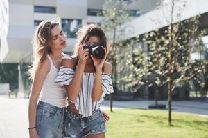 dos bonitas amigas bonitas de la chica con la cámara se toman fotos juntas y caminan por la ciudad