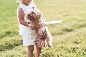 activo y alegre. Sonriente niña alegre sosteniendo perrito y jugando con él afuera en el campo foto