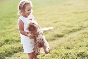Sonriente niña alegre sosteniendo perrito y jugando con él afuera en el campo foto