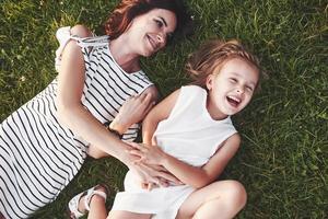 jugando y sonriendo. Vista superior de los niños y la madre que se acuestan en la hierba llena de sol y mirándose foto