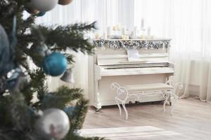 decoración de año nuevo. árbol de navidad cerca de piano blanco en el fondo de la ventana foto