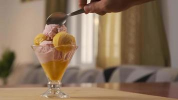 una mano de hombre sosteniendo una cuchara mientras come delicioso y sabroso helado en una taza de vidrio. concepto de verano y azúcar. video